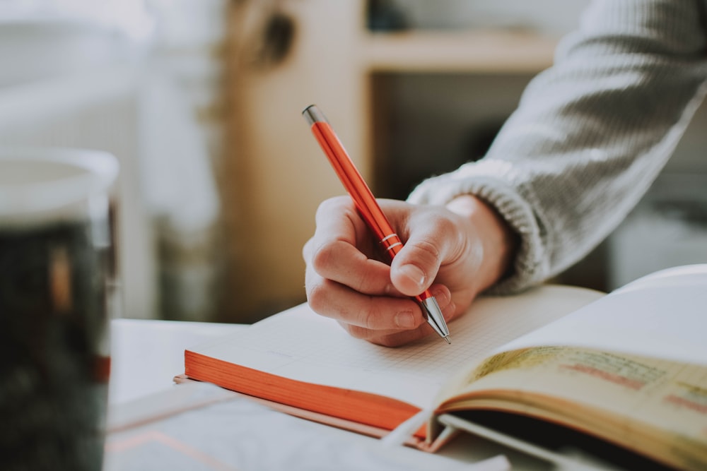 Persona che tiene sulla penna rossa mentre scrive sul libro