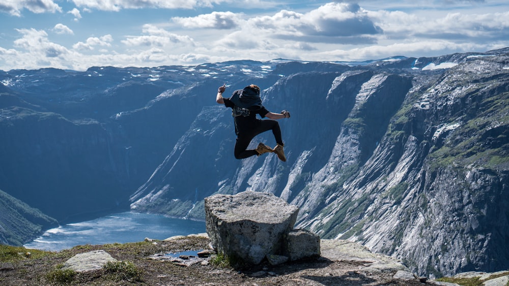 person jumping at the peak of mountain