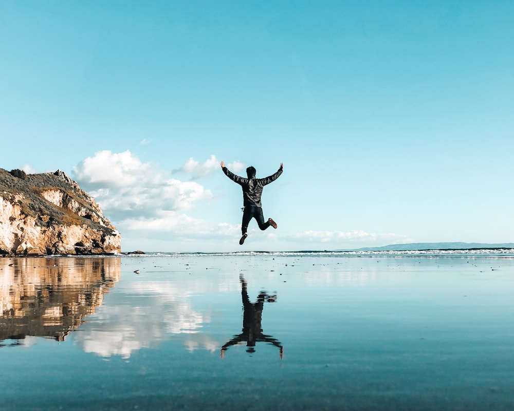 man jumping on top of body of water under blue sky