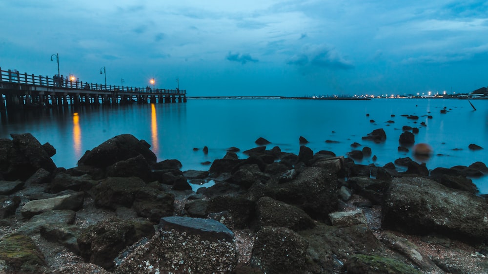 gray rocks beside calm body of water and bridge