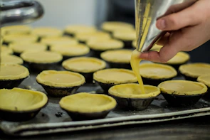 Hands carefully piping cream onto a delicate tart in a cozy kitchen setting