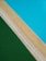 A composition of three distinct elements: a bright blue tiled surface representing a swimming pool, bordered by a narrow slab of beige concrete and a section of vibrant green artificial grass next to a drainage grill.