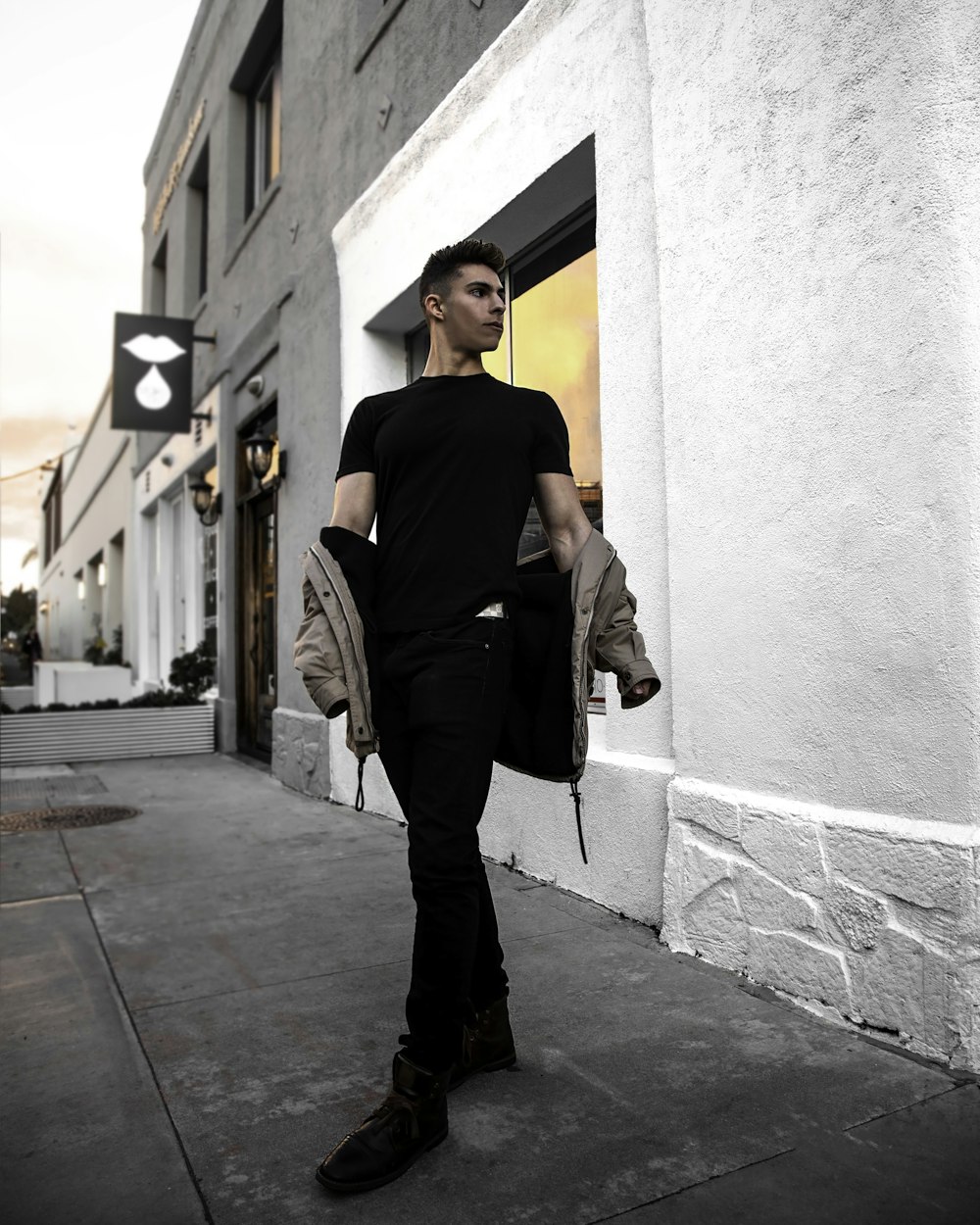 man in black shirt and gray pants leaning on wall