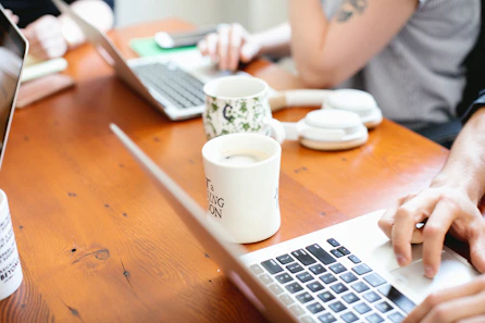 two ceramic mugs on table and two person using laptop