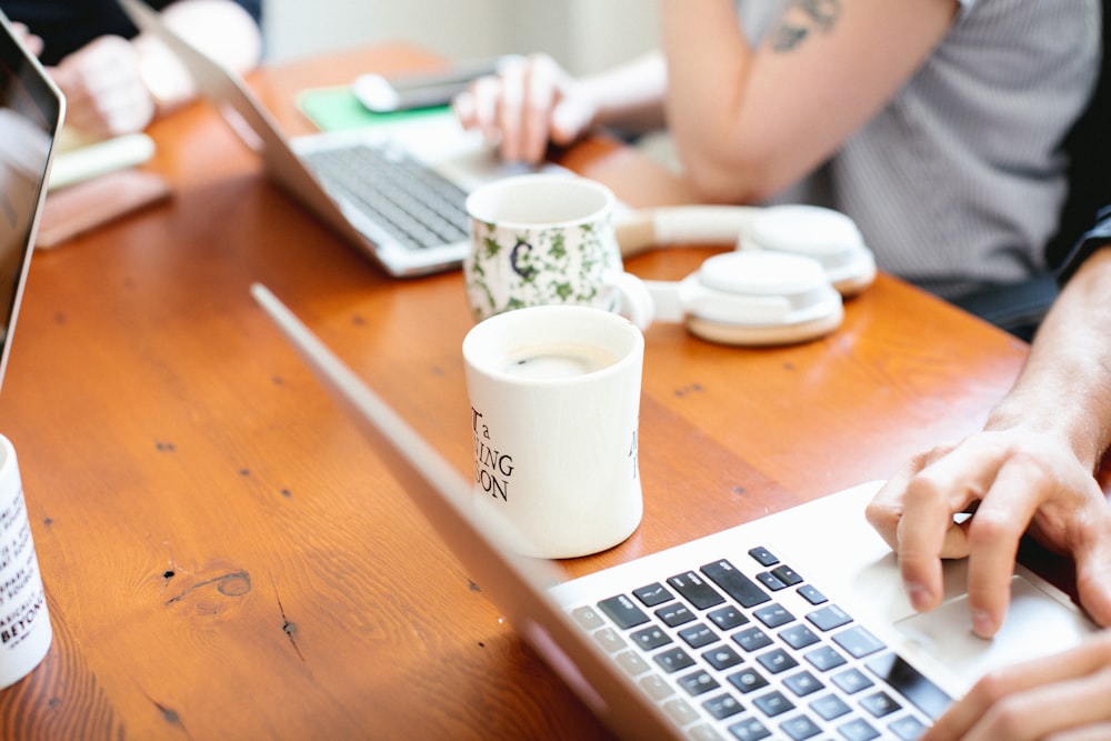 two ceramic mugs on table and two person using laptop
