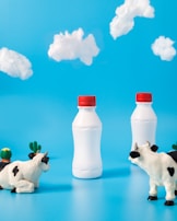 two black-and-white dairy cows looking on white bottles