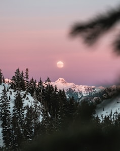 the sun is setting over a snowy mountain