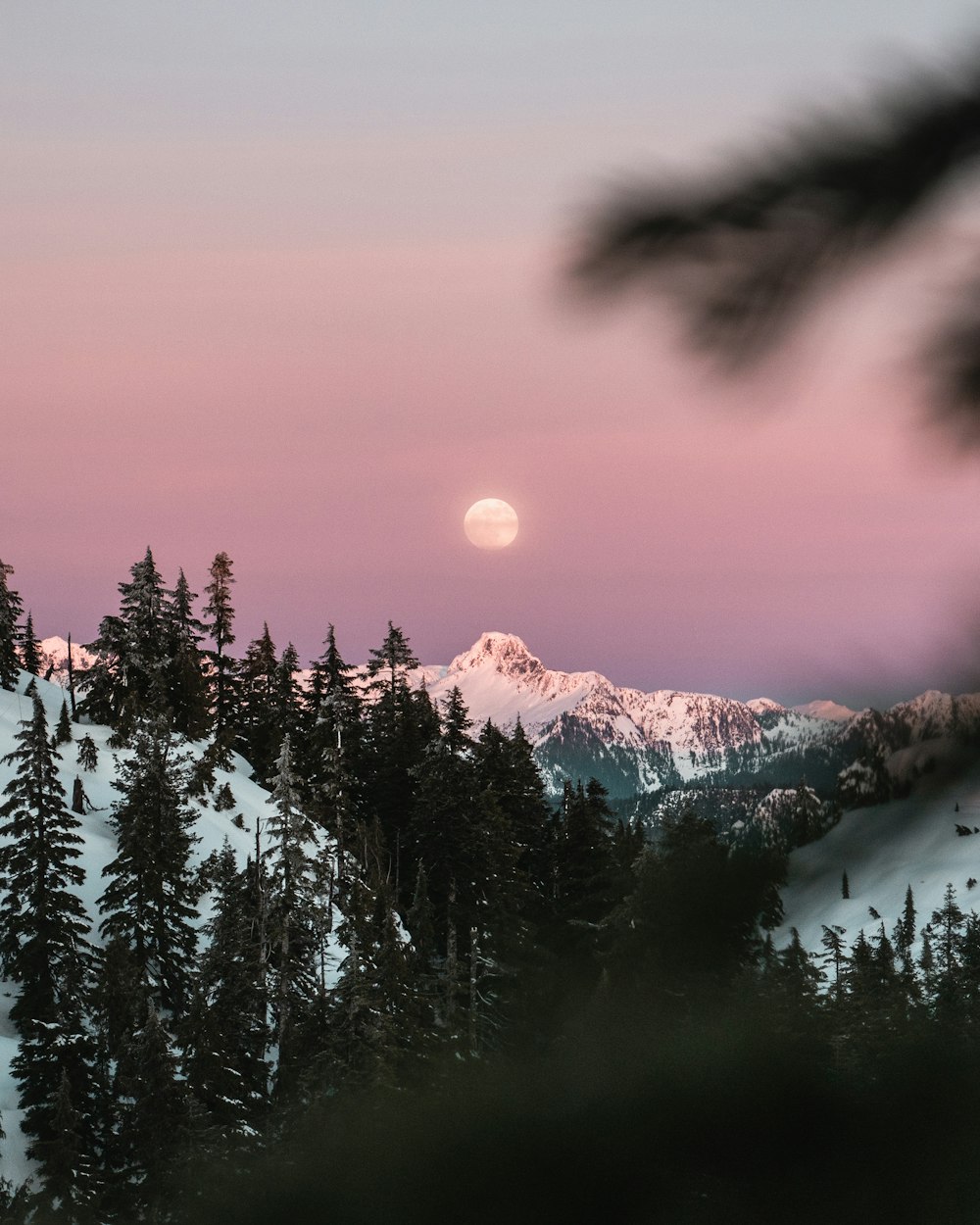 the sun is setting over a snowy mountain