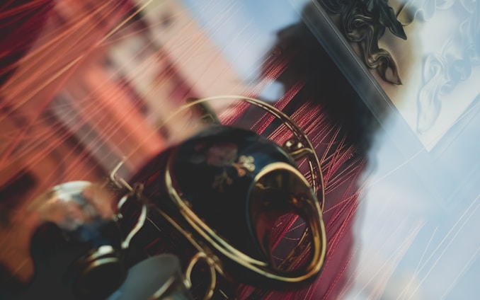 An artistic composition features a reflective surface with blurred objects, including a decorative vase with floral patterns, and red curtains creating a dynamic background.