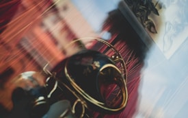An artistic composition features a reflective surface with blurred objects, including a decorative vase with floral patterns, and red curtains creating a dynamic background.