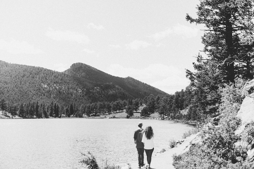 fotografia em tons de cinza do casal caminhando em estrada de terra perto do corpo de água