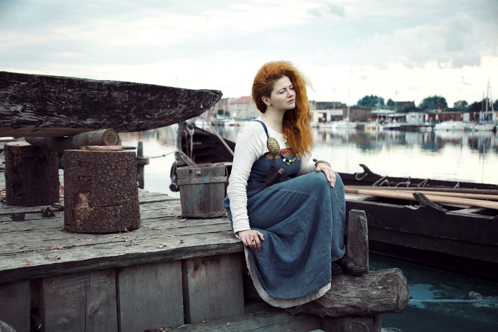 Mujer en vestido azul sentada en muelle marrón