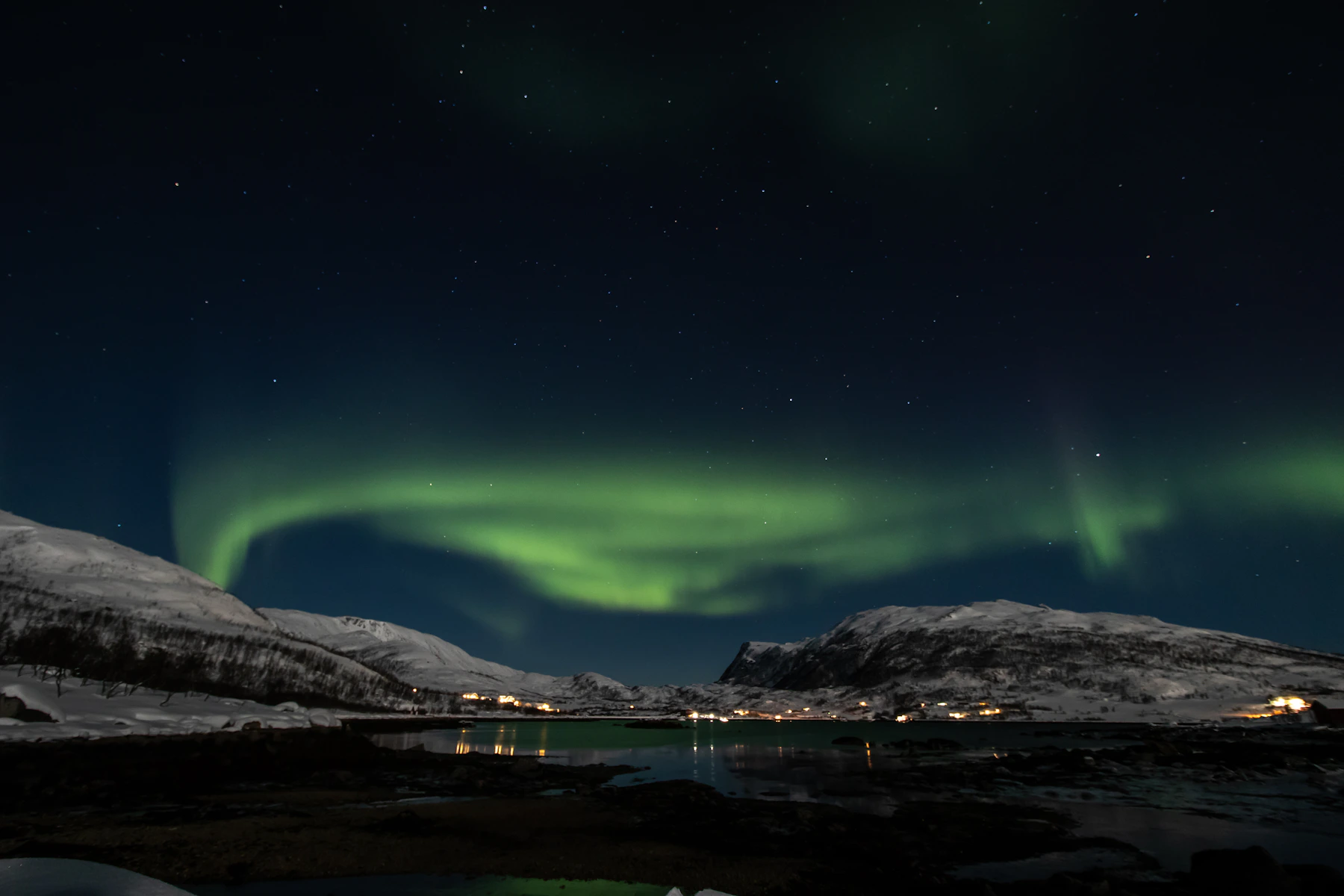 The aurora borealis glowing above mountains and water near Tromsø