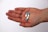 A hand is holding three capsules that are half blue and half white, set against a plain white background. The person is wearing a silver ring on the ring finger.