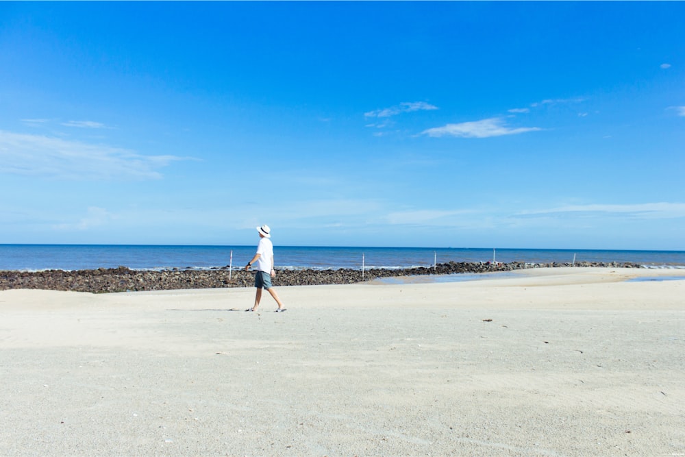 man walking on seashore under blue sky