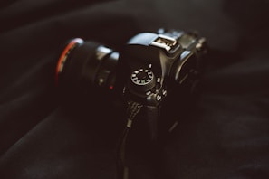 A DSLR camera with a zoom lens resting beside a travel backpack