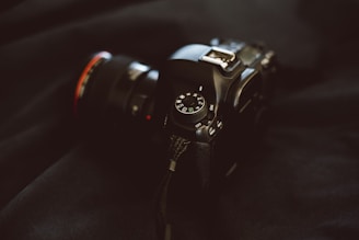 A DSLR camera with a zoom lens resting beside a travel backpack