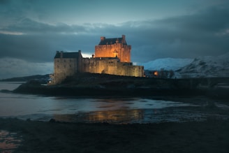 Evening view of a castle illuminated with warm lights, blending with the natural landscape
