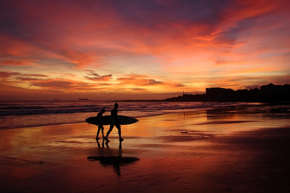 Silueta de hombre que lleva tabla de surf durante la puesta del sol