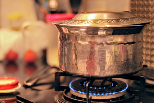 Close-up of a Midaz stainless steel cooker steaming on a gas stove with warm kitchen lighting.