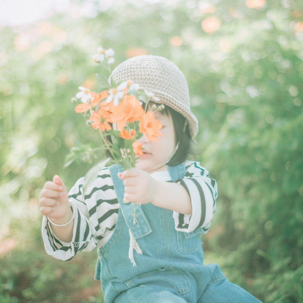 girl wearing hat holding orange flower