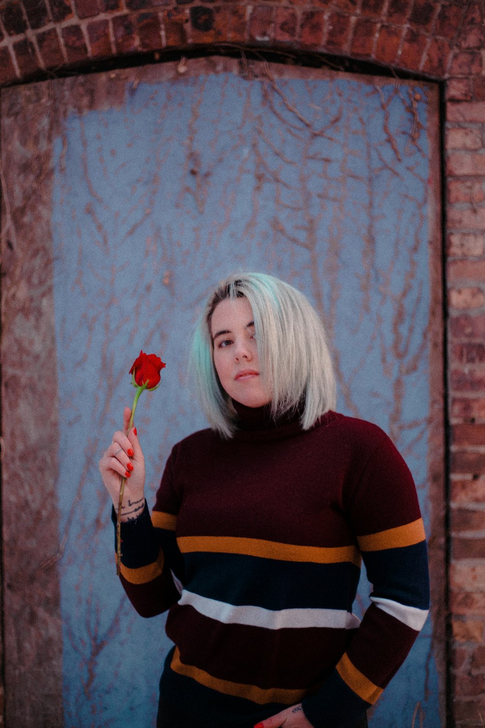 woman in black and orange striped turtleneck sweater holding red rose