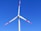 A wind turbine with three white blades, tipped with red, set against a clear blue sky.
