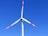 A wind turbine with three white blades, tipped with red, set against a clear blue sky.