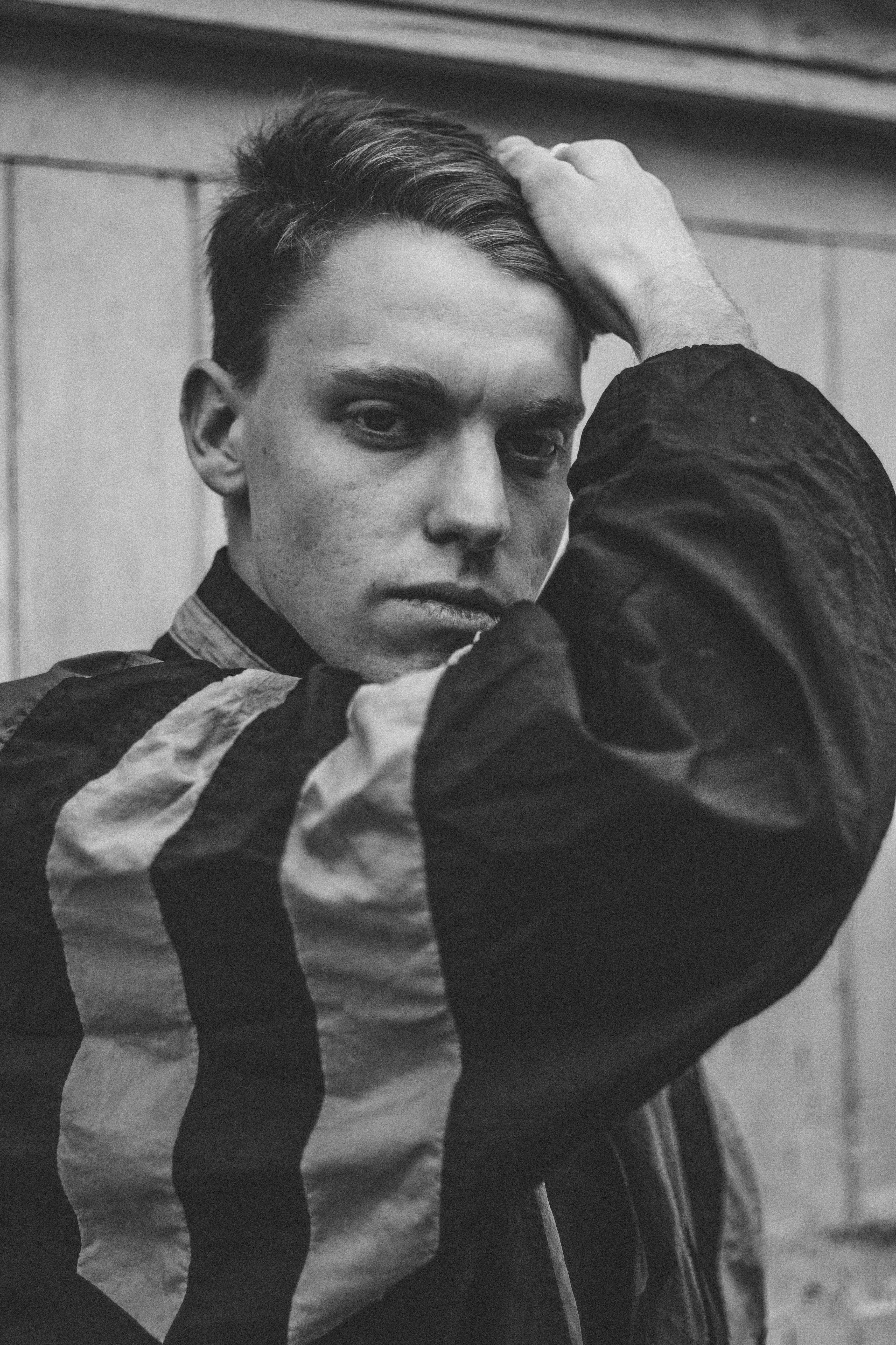man holding hair while standing beside wall