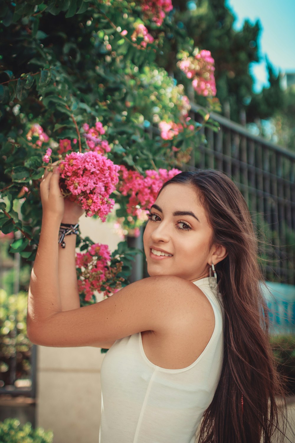 smiling woman in white top grabbing a pink flower during daytime