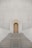 A grand staircase leads up to a large, wooden arched door set into a textured stone wall. The staircase is flanked by rows of vertical, evenly spaced stone columns that create a sense of symmetry and grandeur. The door is ornate, with paneling and large handles.