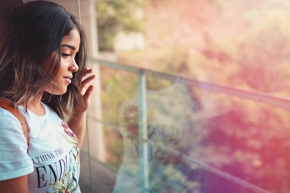 woman in white top leaning by glass wall during daytime