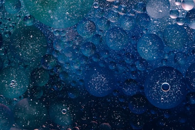 An array of various-sized spheres floating in a fluid, appearing as if viewed under a microscope. The spheres have a translucent quality, with some showcasing subtle color variations and pinpoint reflections, creating a sense of depth.
