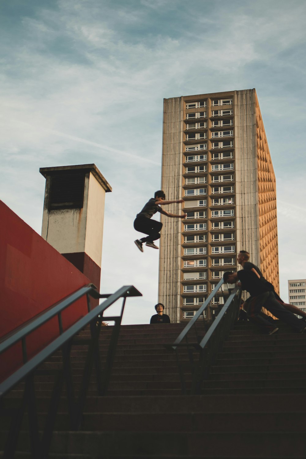 person jumping in front of two person holding railings