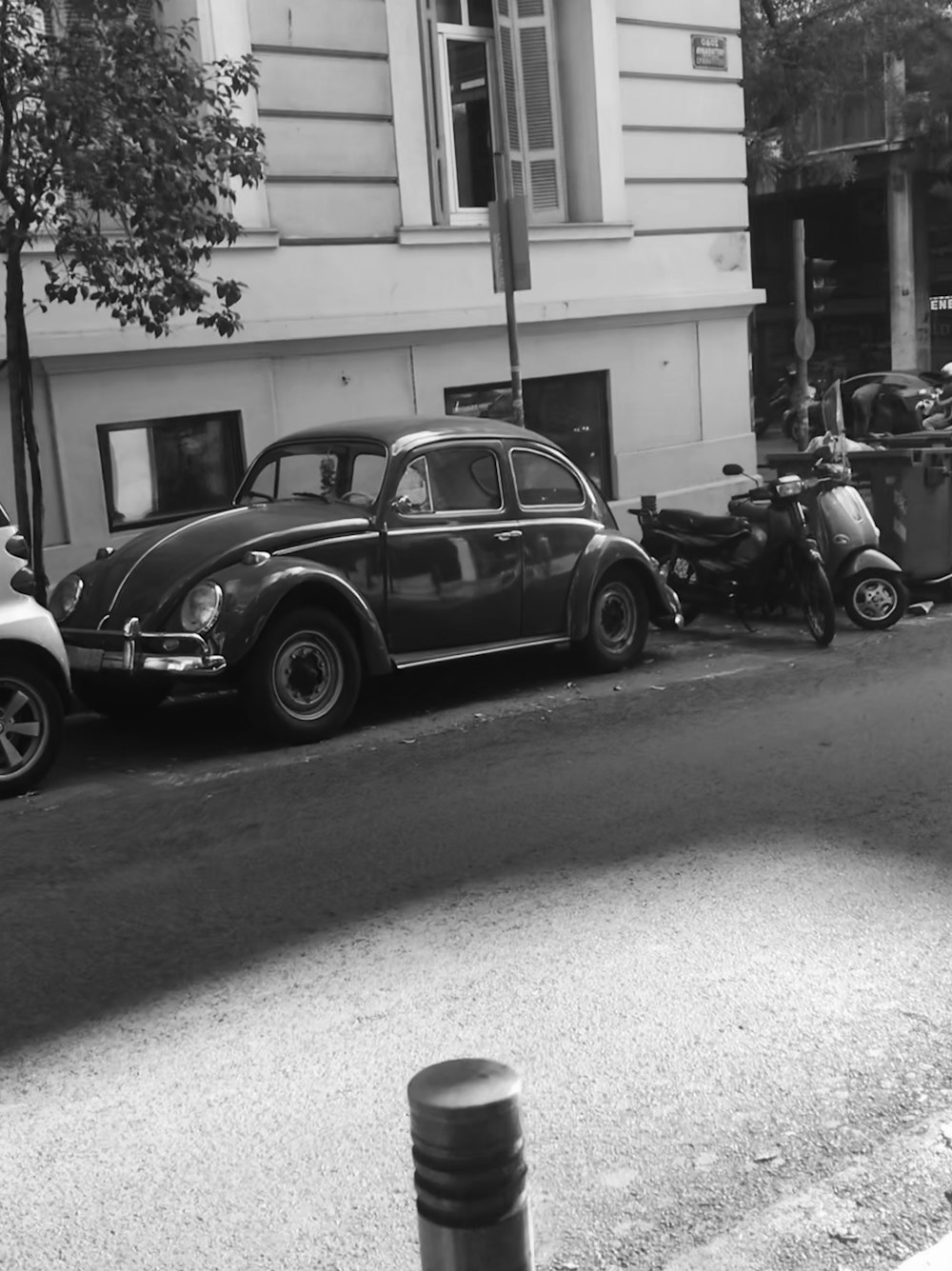 Foto en escala de grises de un Volkswagen Beetle negro estacionado al costado de la carretera