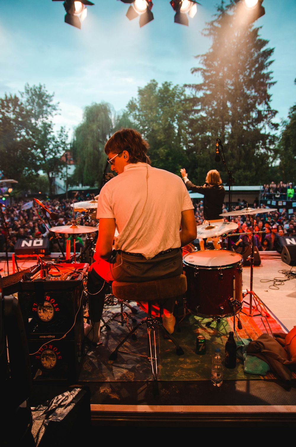 man wearing white top sitting in front of drum kit on concert