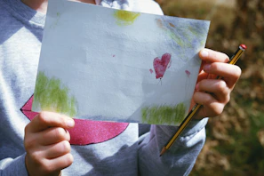 A joyful child holding a handmade heart-shaped craft from a workshop.