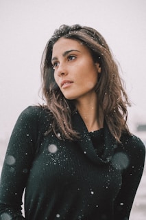 A smiling person wearing a lushknits sweater, standing outside in soft falling snow.