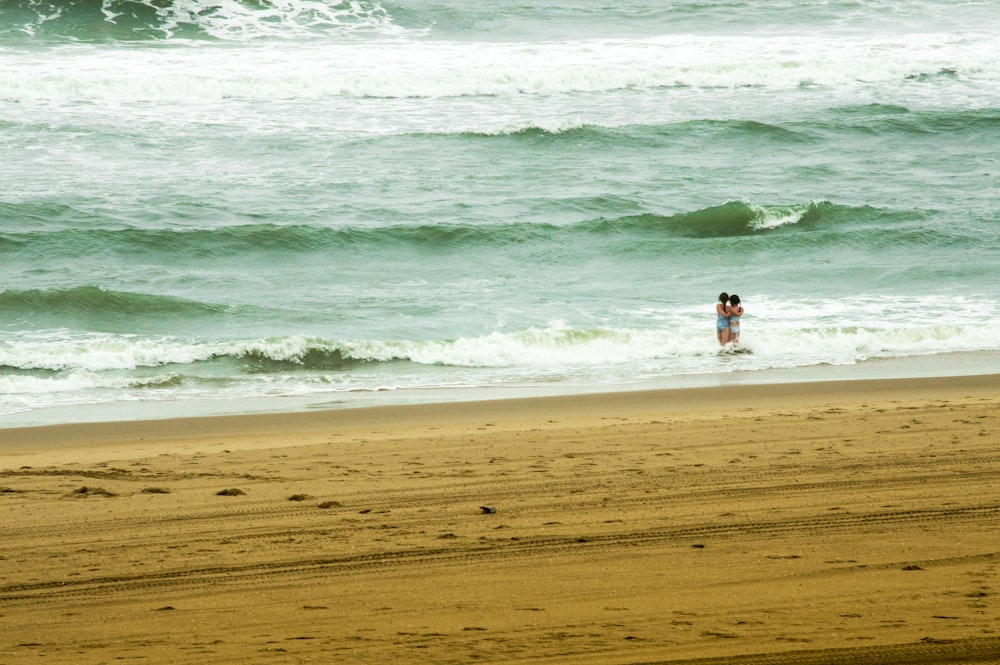 two person standing on sea near shore at daytime