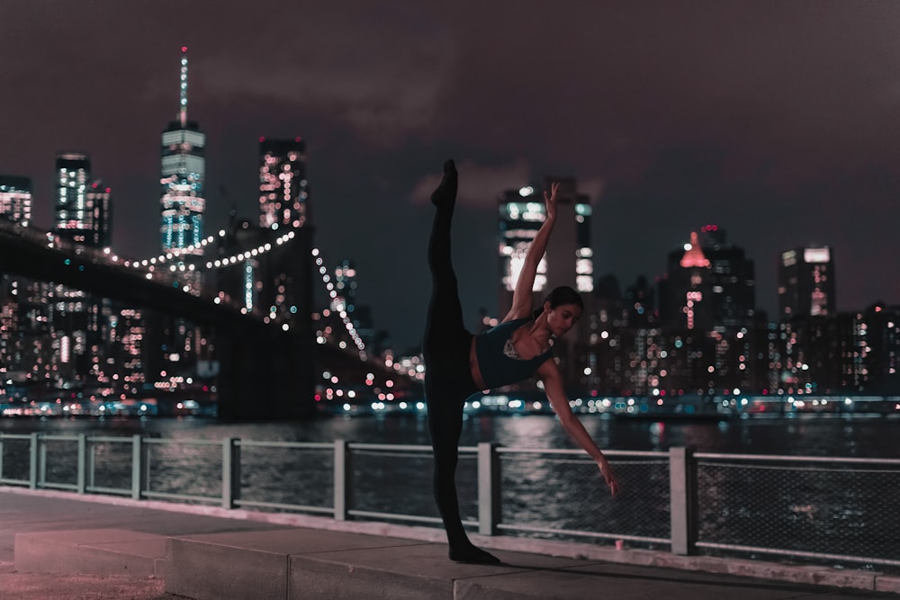 woman in black sports bra and tights doing ballet position on sidewalk during nighttime