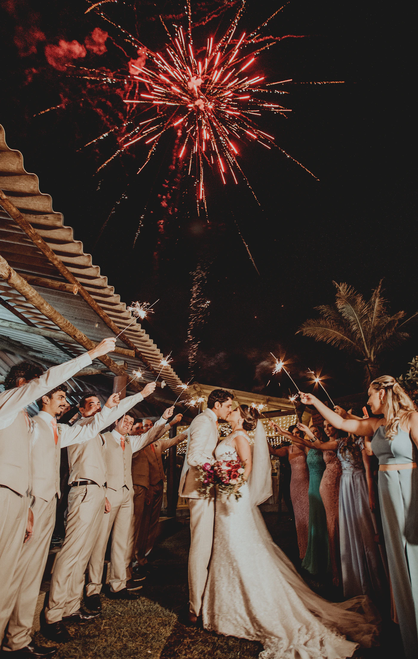 Couple kissing under fireworks at a wedding celebration showing the dramatic exit moment with light and celebration surrounding the newlyweds