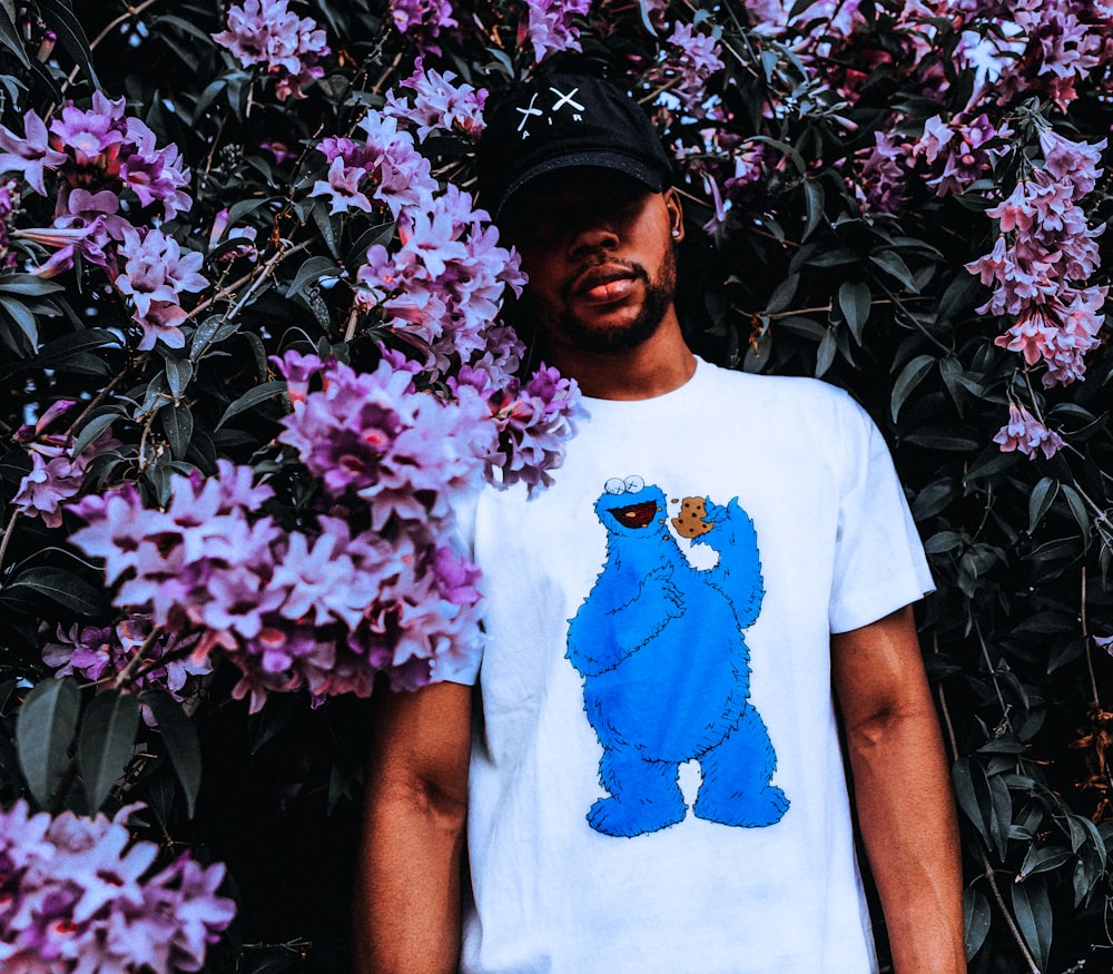man wearing white and blue monster print shirt standing in front of purple flowers