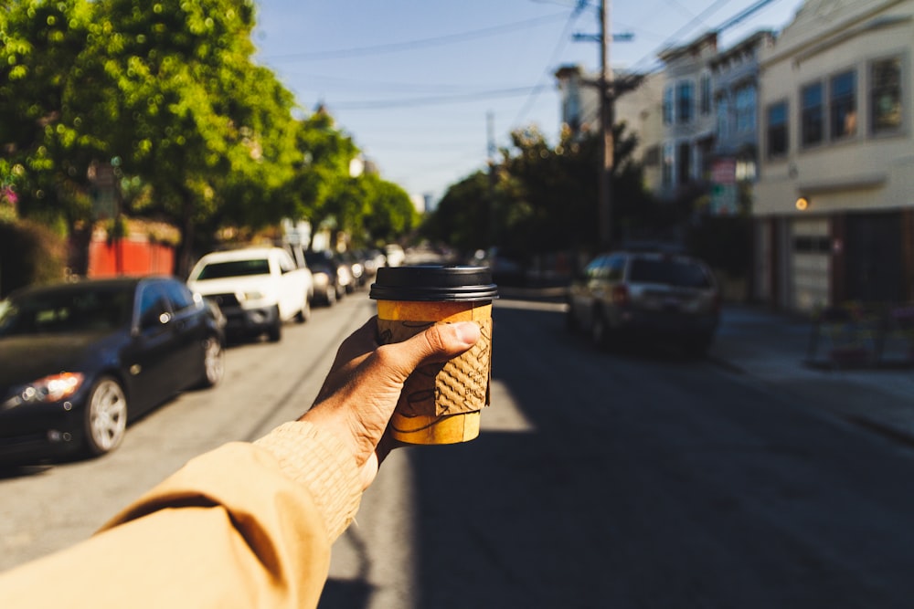person holding brown and black disposable cup on road