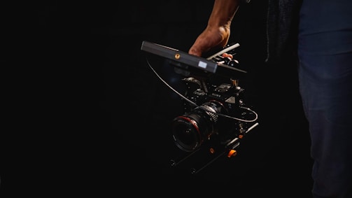 A person is holding a professional camera rig featuring a lens and attached handle, set against a dark background.