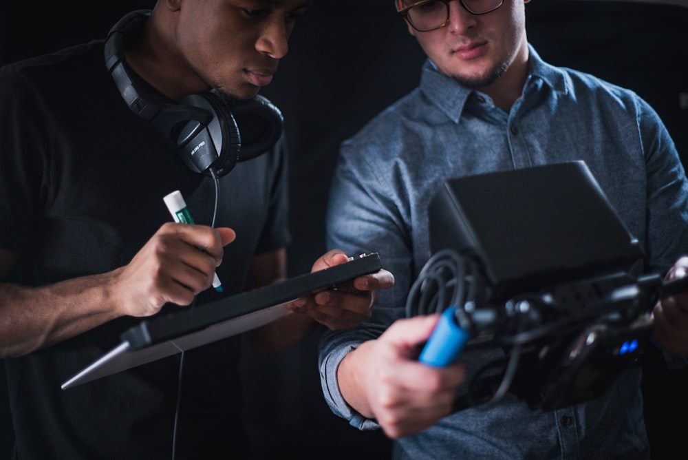 man in black tee shirt holding writing board while other man holding monitoring device