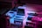 A collection of vintage technology including a small Commodore computer, a Game Boy, an old joystick, and cassette tapes, all arranged under dim, colored lighting creating a nostalgic atmosphere. The overall setup gives a retro vibe with elements from 80s and 90s technology.