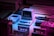 A collection of vintage technology including a small Commodore computer, a Game Boy, an old joystick, and cassette tapes, all arranged under dim, colored lighting creating a nostalgic atmosphere. The overall setup gives a retro vibe with elements from 80s and 90s technology.