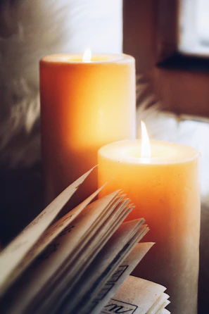 A glowing candle beside an open Bible, casting warm light in a cozy corner.