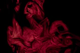 Abstract red and black smoke swirling in a dark room.