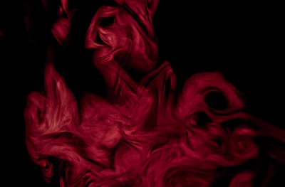 Abstract red and black smoke swirling in a dark room.